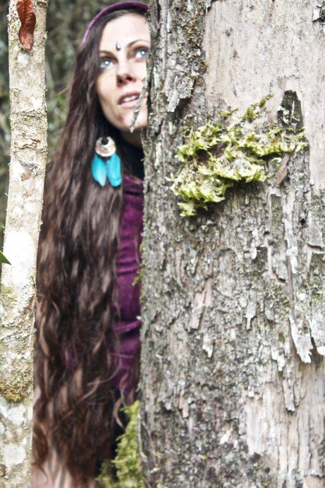 Michela asomándose detrás de un tronco de árbol — Camina con la Elfa